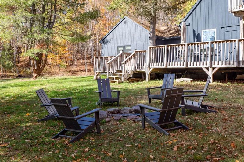 Fire pit seating area with Adirondack chairs in the yard, cottage deck visible
