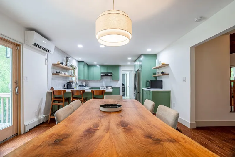 Open-concept dining area leading to a fully equipped kitchen with sage green cabinetry and a cozy breakfast bar. The large wooden table is perfect for gatherings, making this space ideal for both cooking and entertaining.