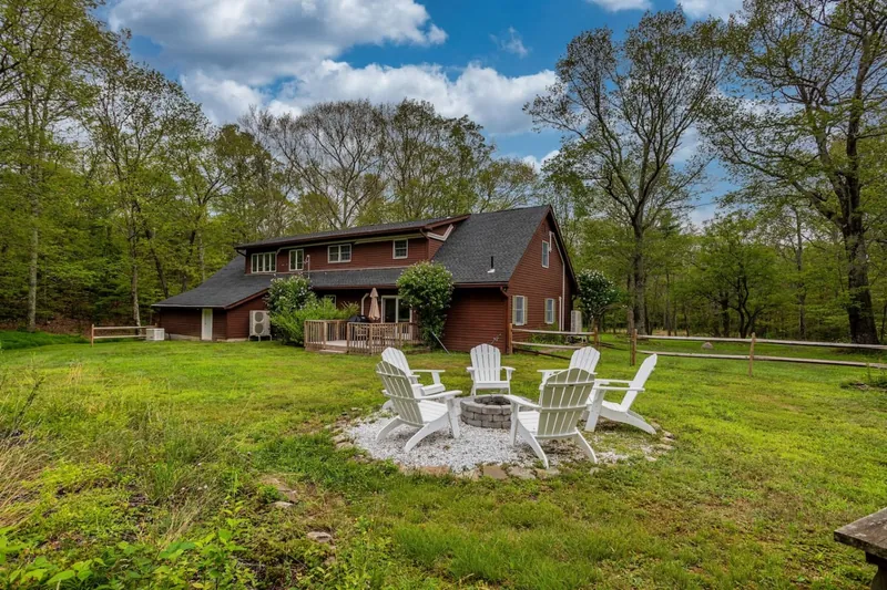 Charming countryside retreat in Saugerties, NY, featuring a spacious yard with a cozy fire pit surrounded by Adirondack chairs. Perfect for relaxing evenings under the stars in a serene natural setting.