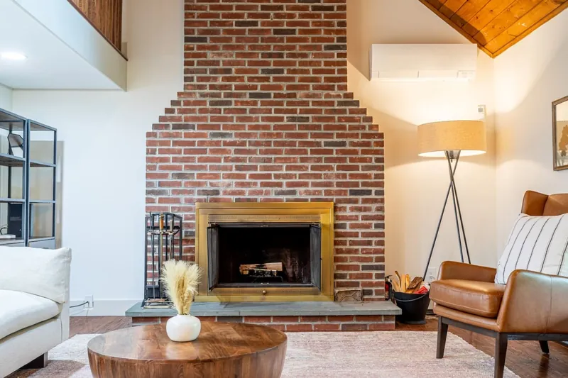 Cozy up by the rustic brick fireplace in this inviting living area. The space features warm lighting, a comfortable leather chair, and modern decor, perfect for relaxing after a day of exploring.