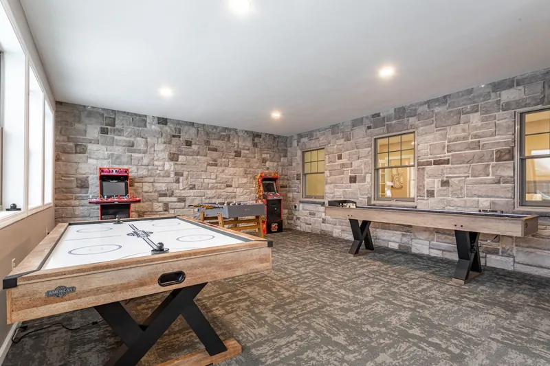 Game room with air hockey, foosball, shuffleboard, two arcade machines, and stone walls